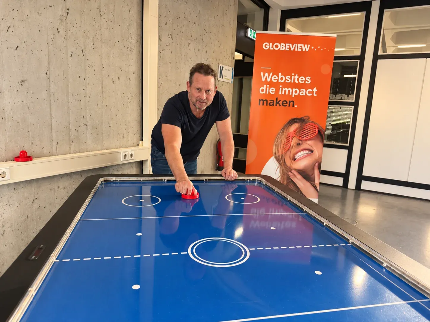 Dennis aan de airhockeytafel in Carbon6, naast de Globeview-banner