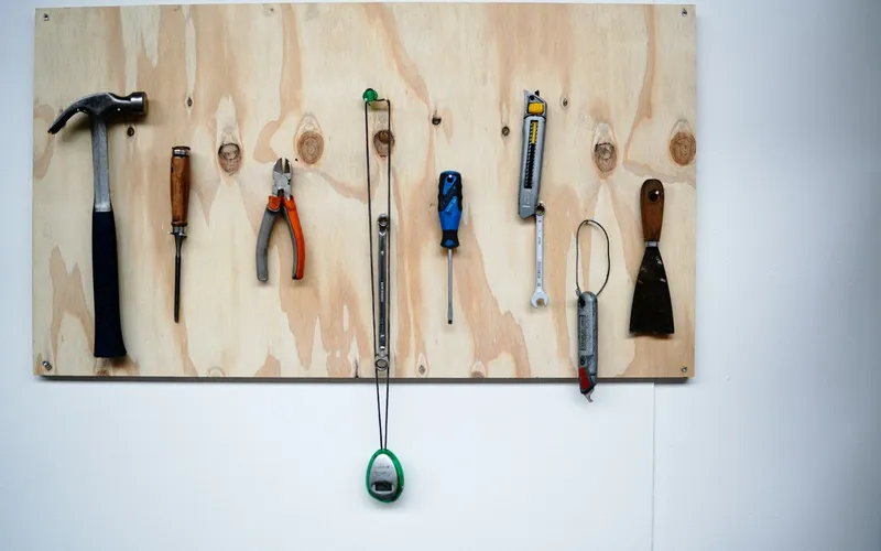 Gereedschap netjes aan een houten plank tegen een witte muur
