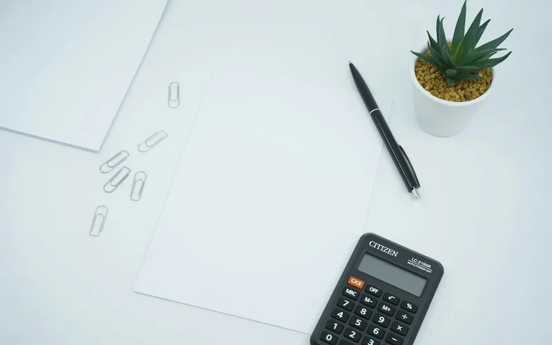 Rekenmachine en pen op wit papier naast een plantje