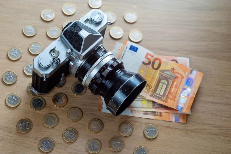 uro banknotes, coins and a camera on a light wooden background.